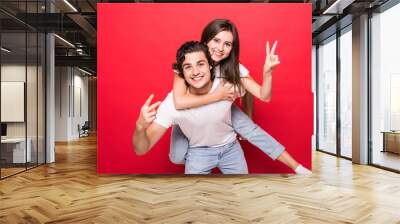 Handsome young man giving piggy back to his girlfriend on red background Wall mural